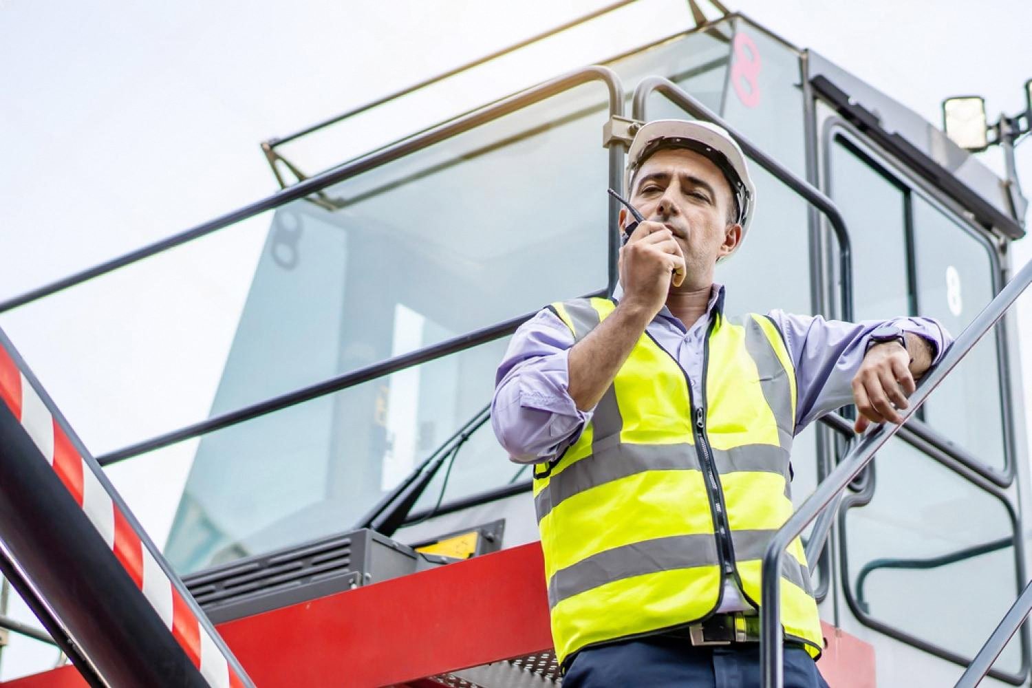 Supervisor on a container handler cab speaking on a radio to coordinate vessel and truck movements